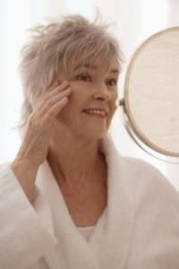 Older woman looking into a mirror touching her face and smilling